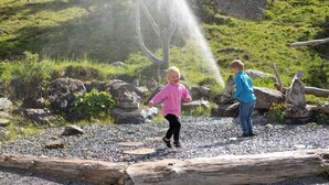 Two children playing near a water feature in a natural setting with rocks and logs. - Cosy Chalet with Panoramic View, Sun Terrace and Free Summer Mountain Cable Car (Ladis)