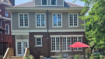 Une maison à deux étages avec un porche à l’avant, un parasol rouge et une façade en briques.