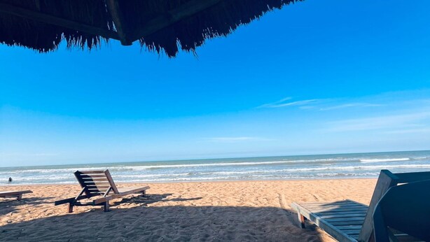 A beach with two wooden lounge chairs and a thatched roof structure. - Pousada Jubarte (Serra)