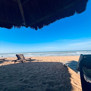 A beach with two wooden lounge chairs and a thatched roof structure. - Pousada Jubarte (Serra)