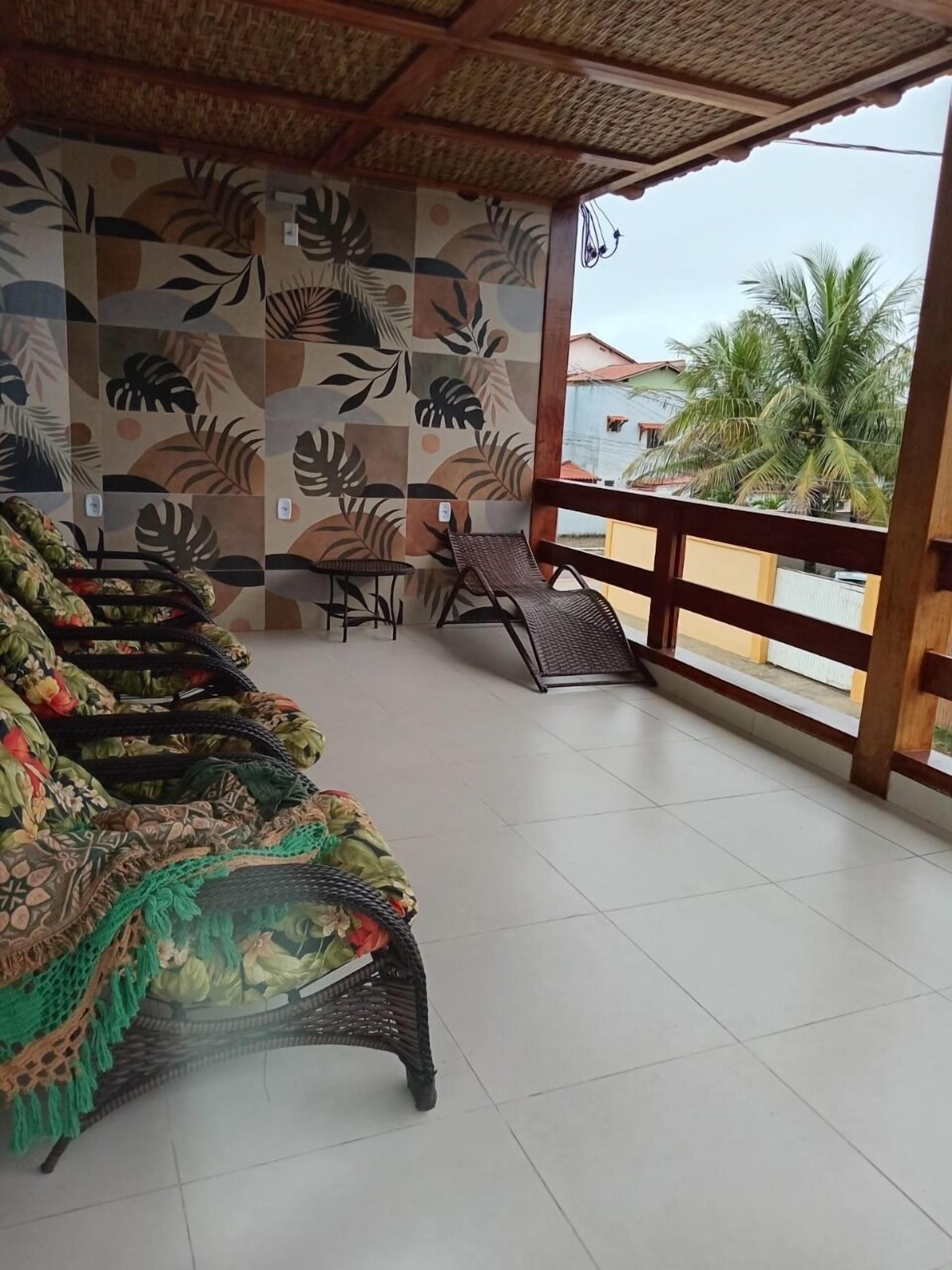 A covered outdoor seating area with a patterned wall, wicker furniture, and a view of palm trees.