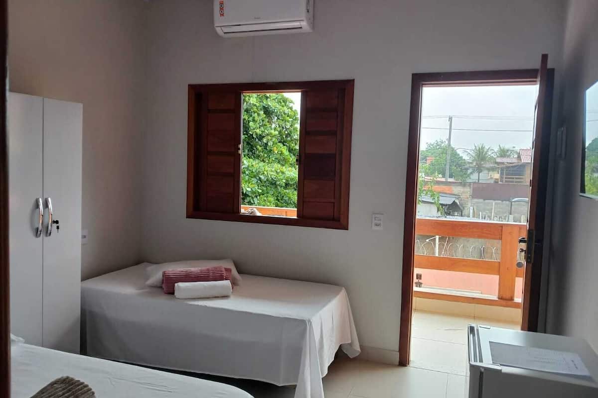 Ein Schlafzimmer mit einem Einzelbett, einem kleinen Tisch, einem Kleiderschrank und einem Fenster mit Blick auf Grünflächen und Gebäude.
