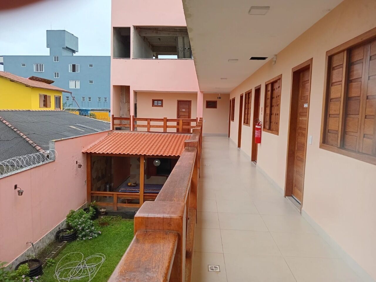 Un pasillo con bancos de madera, un pequeño jardín y un edificio con fachada rosa y puertas de madera.