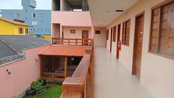 Un pasillo con bancos de madera, un pequeño jardín y un edificio con fachada rosa y puertas de madera.