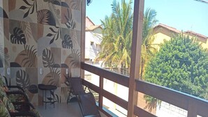 A balcony with wicker furniture, a tiled floor, and a view of palm trees and buildings. - Pousada Jubarte (Serra)