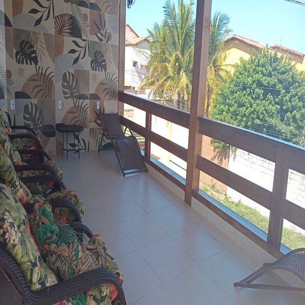 A balcony with wicker furniture, a tiled floor, and a view of palm trees and buildings. - Pousada Jubarte (Serra)