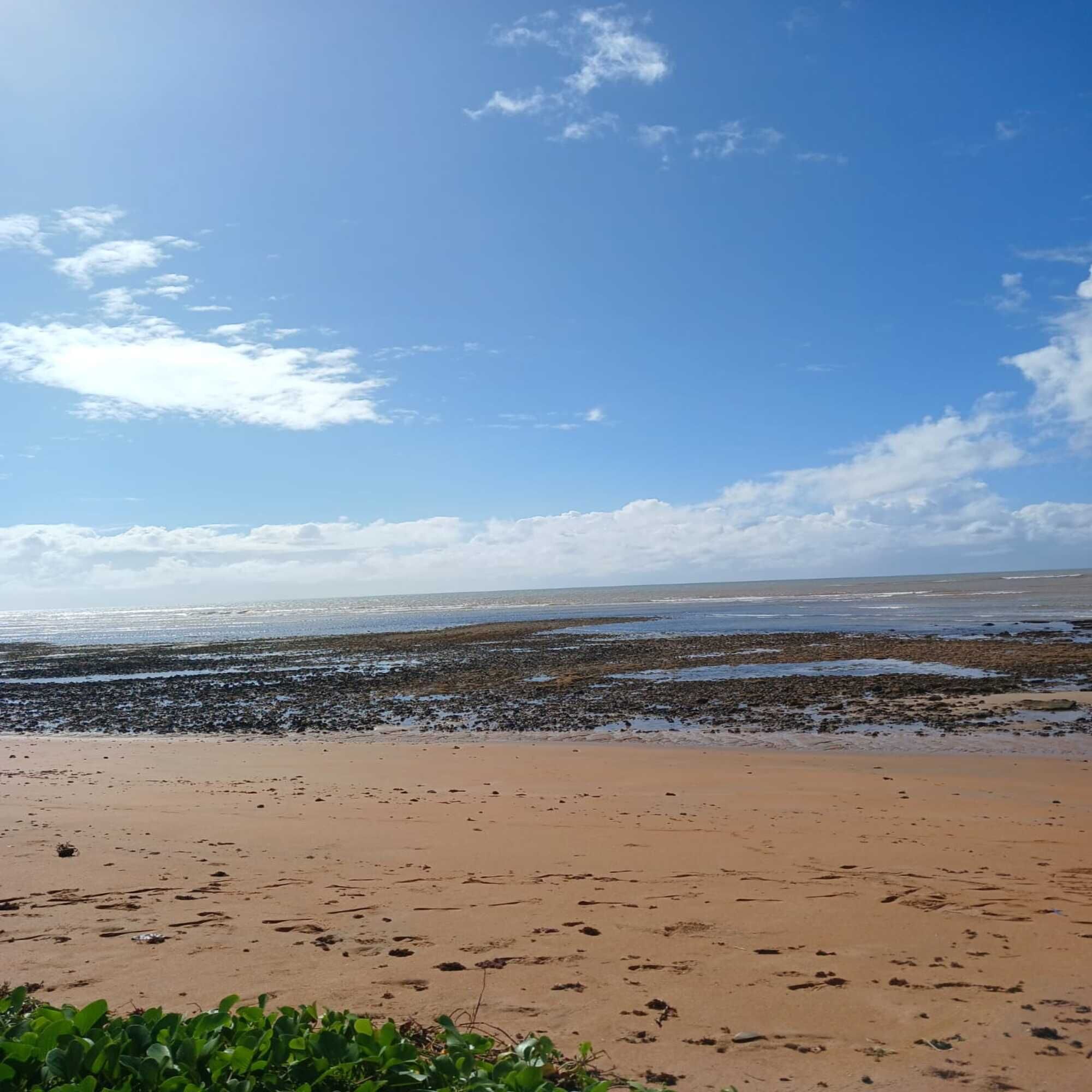 Uma praia com céu claro e algumas nuvens.