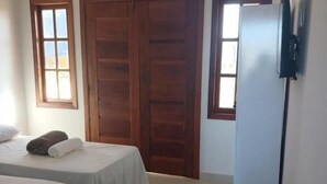 A hotel room with two single beds, a wardrobe, a television, and an air conditioning unit. - Pousada Jubarte (Serra)