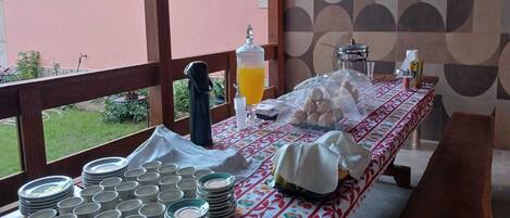 A breakfast setup with plates, cups, and a juice dispenser on a table with a patterned tablecloth.
