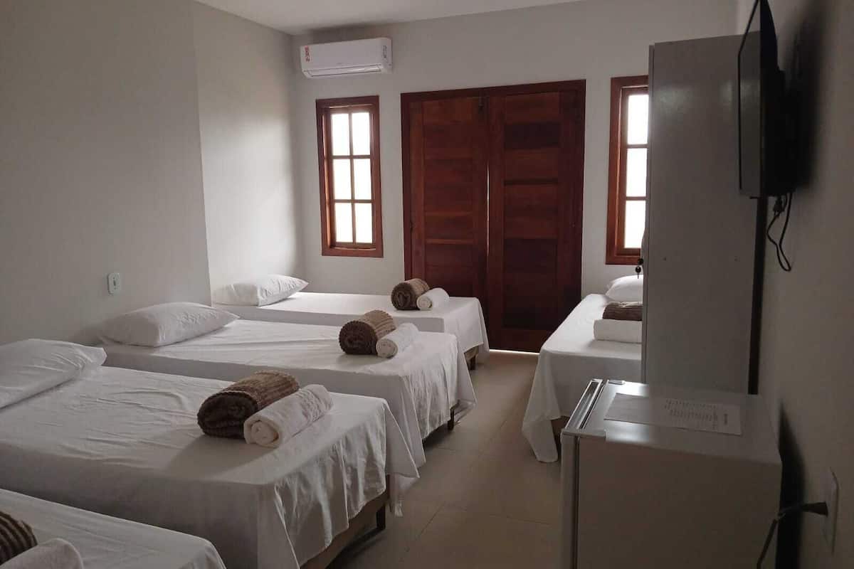 Ein Hotelzimmer mit drei Einzelbetten, einem Fernseher und einer Holztür.