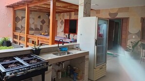 A kitchen with a gas stove, sink, and refrigerator. There is a wooden pergola structure and a patterned wall in the background. - Pousada Jubarte (Serra)