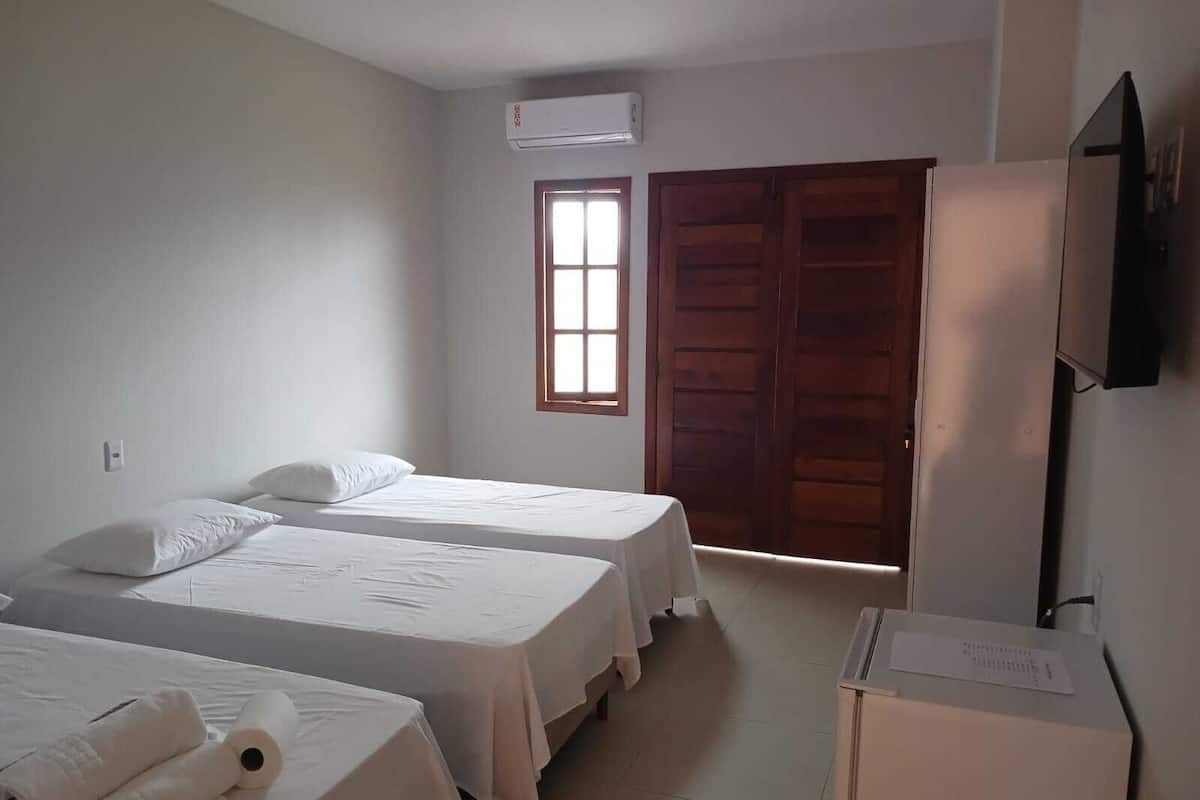 Ein Hotelzimmer mit zwei Betten, einem Fenster, einer Klimaanlage und einem Fernseher an der Wand.