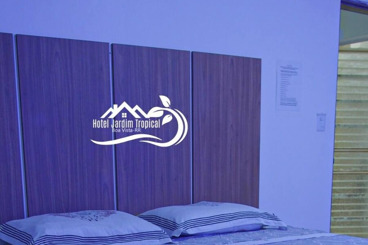 Ett hotellrum med en säng, en sänggavel och en vägg med en logotyp.