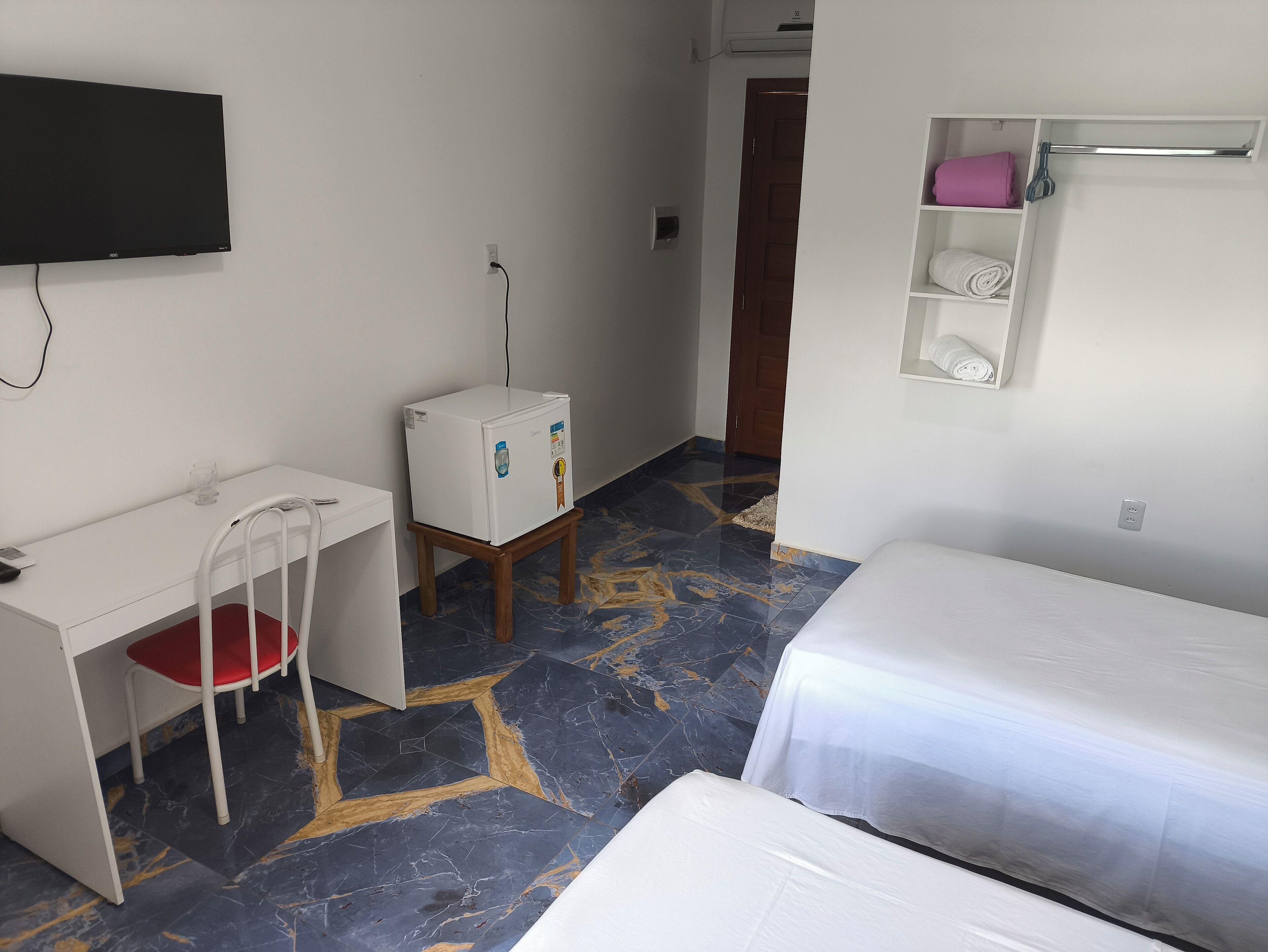 A hotel room with a desk, chair, bed, and a small refrigerator.