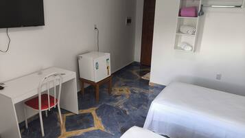 A hotel room with a desk, chair, bed, and a small refrigerator.