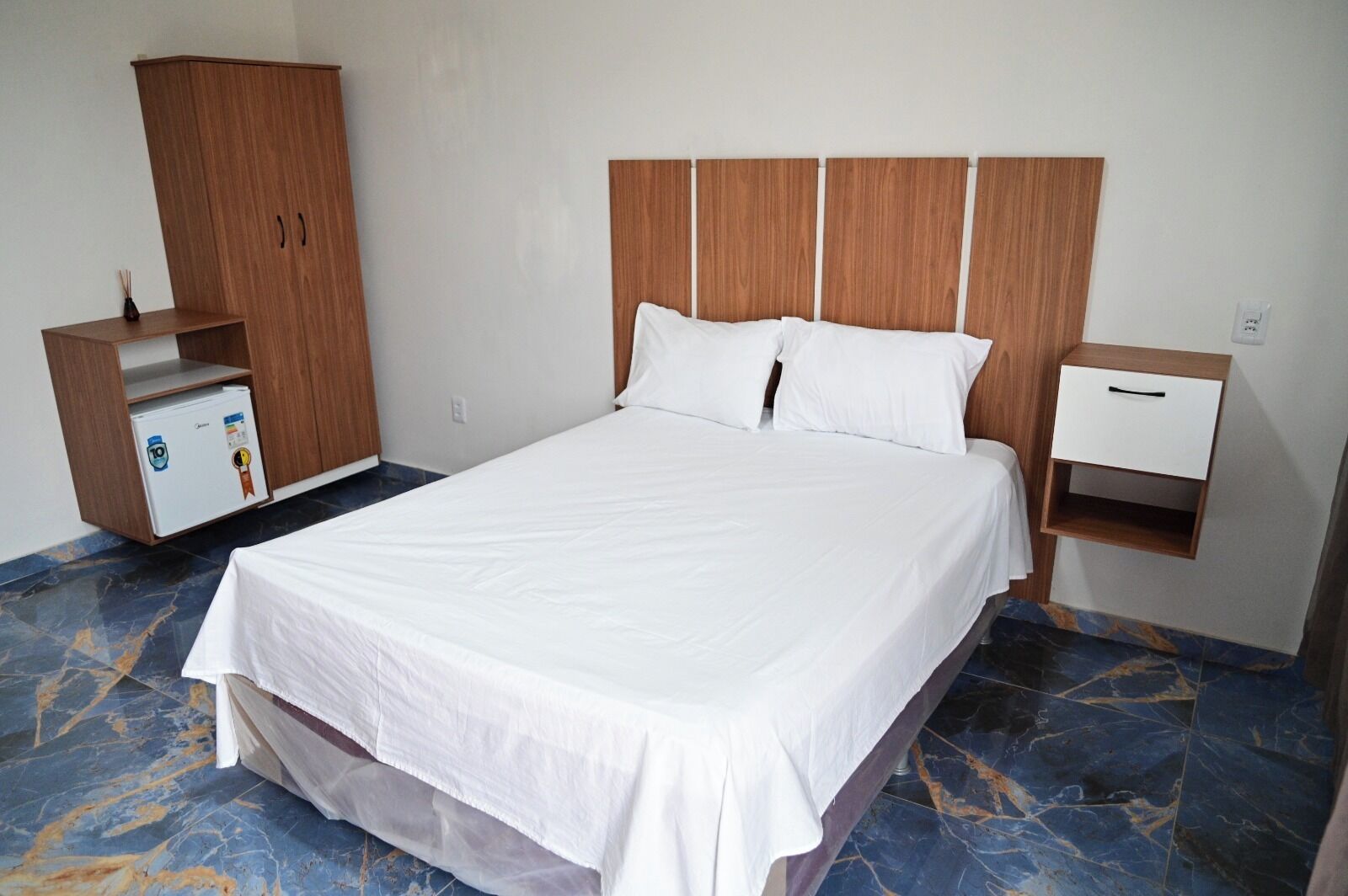 Ein Hotelzimmer mit einem großen Bett, einem Holzschrank, einem kleinen Schreibtisch mit Schublade und einer Minibar.