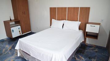 Ein Hotelzimmer mit einem großen Bett, einem Holzschrank, einem kleinen Schreibtisch mit Schublade und einer Minibar.
