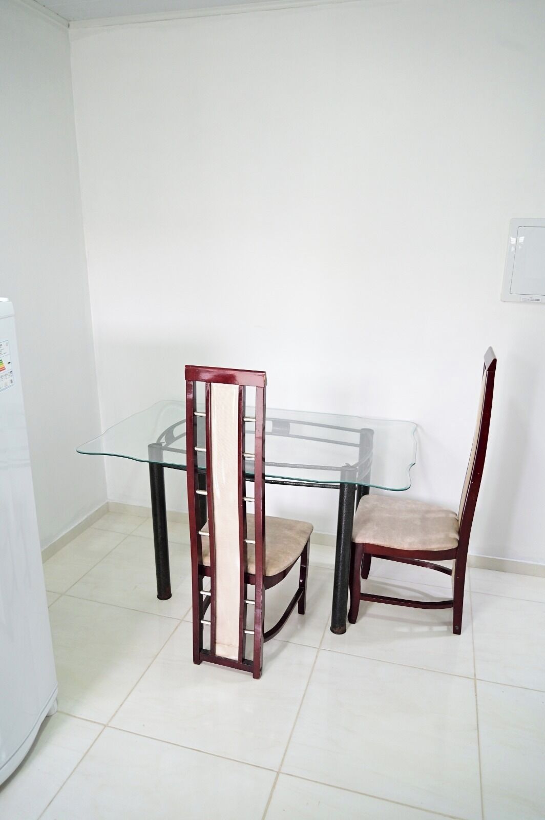 A dining area with a glass table and two wooden chairs.