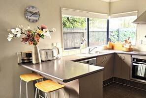 Cocina moderna con una isla central, taburetes de bar, un reloj y una ventana con vistas a zonas verdes.