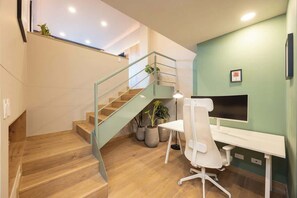 A modern office space with a wooden staircase, a white desk, and a computer monitor.
