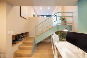 A modern interior with a wooden staircase, a white bench, and a flat-screen TV.