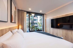 A modern hotel room with a large bed, a TV mounted on the wall, and a view of the outside balcony.