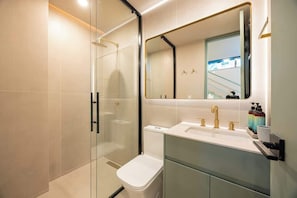 A modern bathroom with a glass shower enclosure, a white toilet, a large mirror, and a vanity with a sink and two faucets.