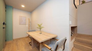 Un comedor con una mesa y sillas de madera, un jarrón con una planta, y una escalera a la derecha.