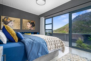 A bedroom with a large bed, a view of the outdoors, and artwork on the wall. - Red River Valley - Three Bedroom House, Sleeps 6 (Cape Town)