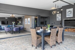 A modern dining area with a dark table and patterned chairs, a kitchen in the background, and artwork on the walls. - Red River Valley - Three Bedroom House, Sleeps 6 (Cape Town)