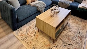 A modern living room with a dark blue sectional sofa, a wooden coffee table, and a patterned rug.
