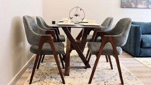 A dining area with a glass table, four grey upholstered chairs, and a blue sofa in the background.