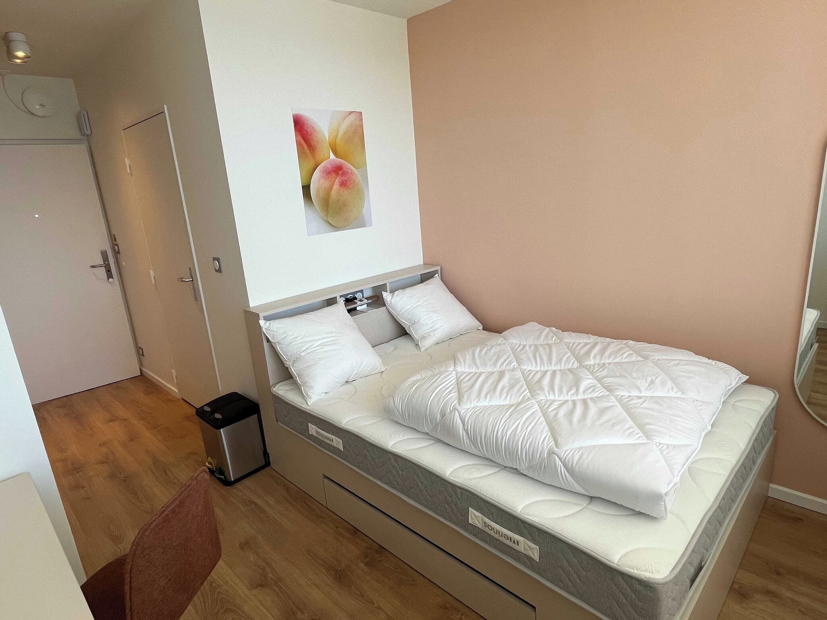 A neatly arranged bedroom with a bed, a small trash bin, and a door.