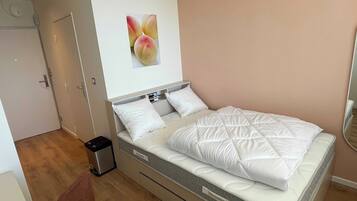 A neatly arranged bedroom with a bed, a small trash bin, and a door.
