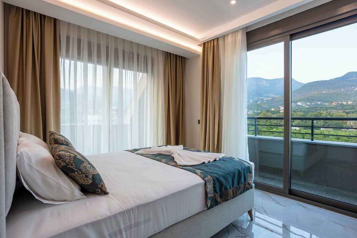 A hotel room with a large bed, a view of the mountains, and a balcony.