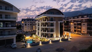 Un hotel de varios pisos con piscina, rodeado de otros edificios y un paisaje montañoso.