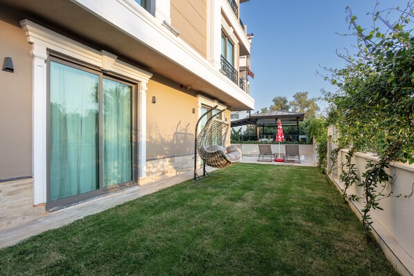 A modern building with large sliding glass doors, a hanging chair, and a patio area with a table and chairs.