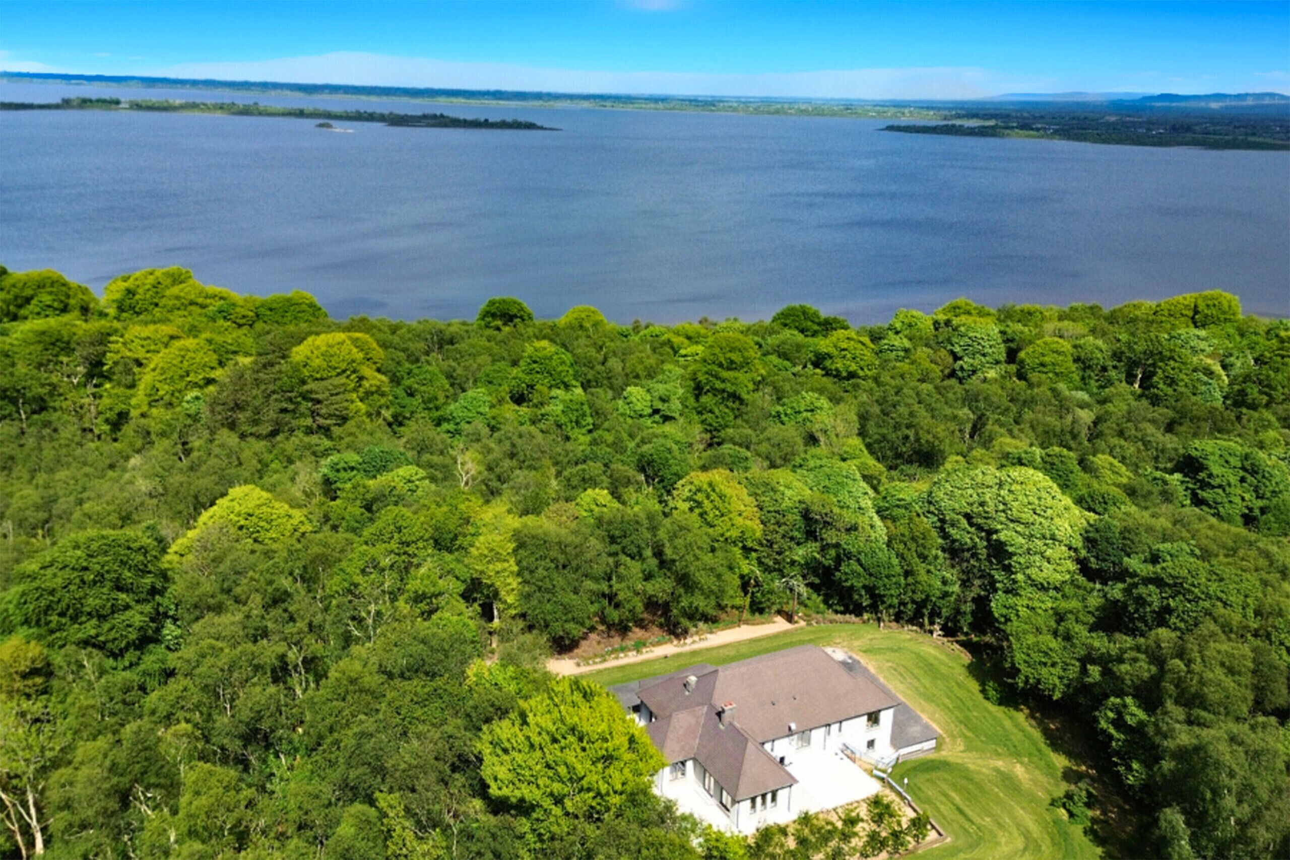 A large house surrounded by dense forest with a view of a lake.