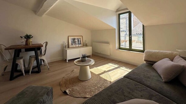 A cozy loft apartment with a dining area, a sofa, and a large window providing natural light. - Studio under the roof - Marché (LA ROCHELLE)