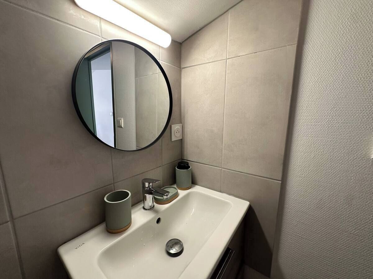 Un bany amb un lavabo blanc, un mirall rodó i una làmpada sobre el mirall.