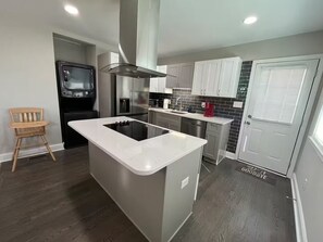 A modern kitchen with a central island, stainless steel appliances, and a wooden chair.