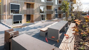 A modern building with a wooden facade, balconies, and a paved outdoor area with benches. - VISIMO Apartments Zurich Airport (Kloten)