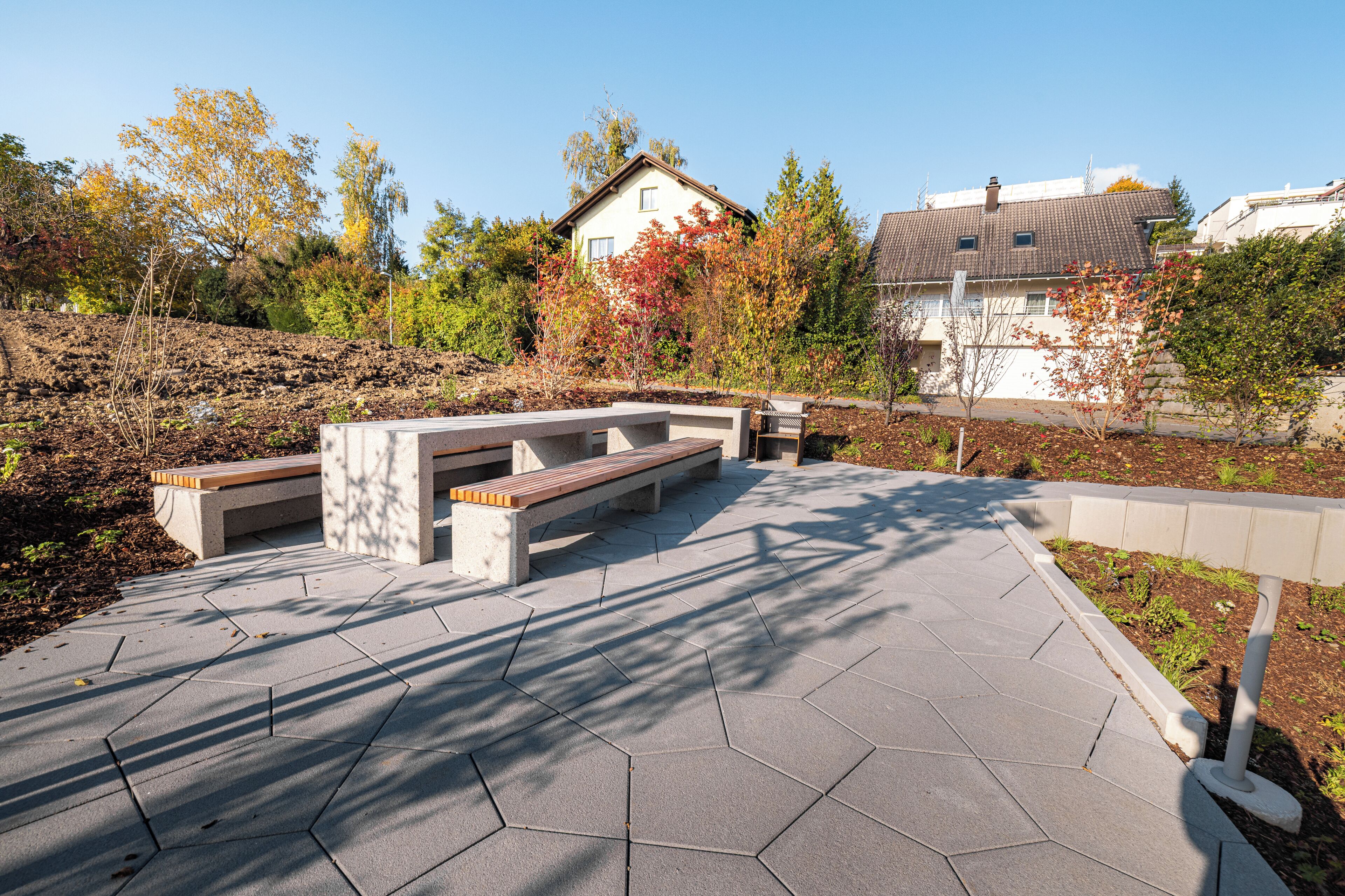 A hexagonal paved outdoor area with benches and a small garden.