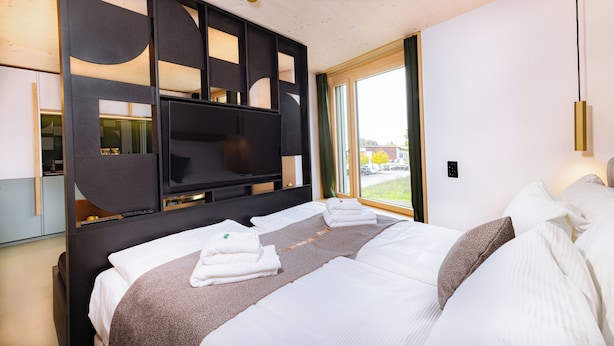 A modern hotel room with a large bed, a flat-screen TV, and a view of the outdoors. - VISIMO Apartments Zurich Airport (Kloten)