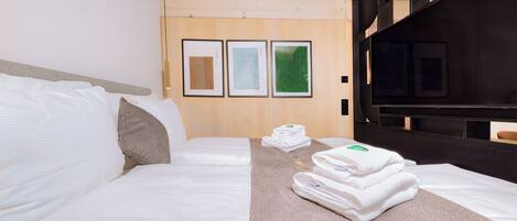 Ein Hotelzimmer mit zwei Betten, einem Fernseher und gerahmten Kunstwerken an der Wand.