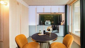 A compact kitchen with modern appliances, a dining table with two chairs, and a large window with curtains. - VISIMO Apartments Zurich Airport (Kloten)