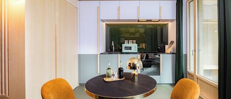 A compact kitchen with modern appliances, a dining table with two chairs, and a large window with curtains.