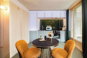 A compact kitchen with modern appliances, a dining table with two chairs, and a large window with curtains. - VISIMO Apartments Zurich Airport (Kloten)