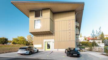 A modern building with a flat roof and a vertical wooden facade. There are two cars parked in front.