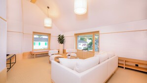 A modern living room with a white sofa, a coffee table, and a bench. There are two windows providing natural light and a view of the outside. - VISIMO Apartments Zurich Airport (Kloten)